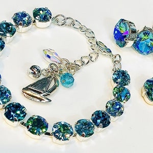 Puede incluir: Un brazalete de plata con un dije de velero y cuentas de cristal azul. Un collar a juego con dos cuentas de cristal azul cuelga de una cadena de plata.