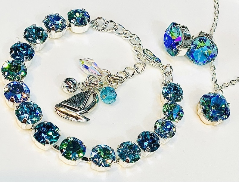 Puede incluir: Un brazalete de plata con un dije de velero y cuentas de cristal azul. Un collar a juego con dos cuentas de cristal azul cuelga de una cadena de plata.