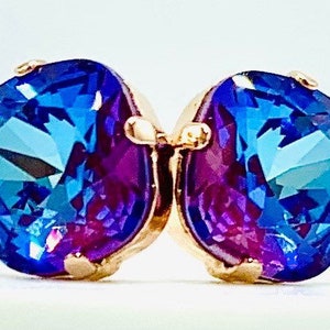Puede incluir: Un par de pendientes de piedras preciosas azules y moradas con engastes de oro. Las piedras preciosas son facetadas y tienen un efecto brillante.