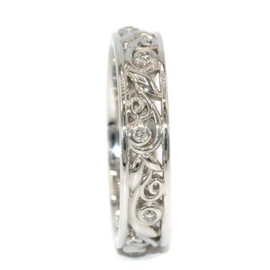May include: A silver band ring with a delicate floral design and small diamonds set in the metal.