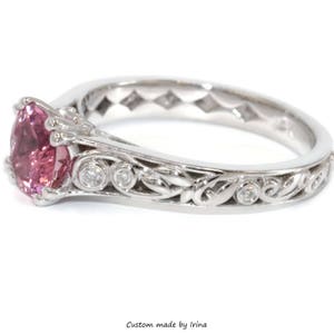 May include: A delicate engagement ring with a pink gemstone surrounded by smaller diamonds. The band is intricately designed with a floral motif.