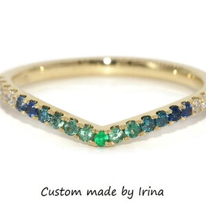 Op de afbeelding: Een gouden ring met een V-vormige rij groene, blauwe en witte edelstenen. De ring is bezet met kleine, ronde stenen.