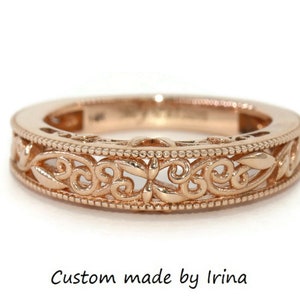 May include: A delicate rose gold band ring with a filigree design. The ring features intricate floral patterns and a delicate beaded edge.