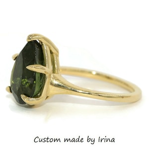 May include: A gold ring with a pear-shaped green gemstone set in a claw setting. The ring is made by Irina.