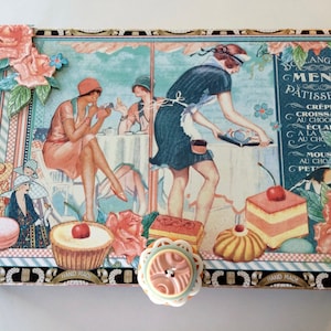 May include: A vintage-style box with a hand-painted design featuring a Parisian cafe scene. The box has a menu for pastries and desserts written in French. The box is decorated with flowers, a woman in a dress, and a pastry chef.