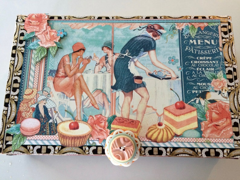 May include: A vintage-style box with a hand-painted design featuring a Parisian cafe scene. The box has a menu for pastries and desserts written in French. The box is decorated with flowers, a woman in a dress, and a pastry chef.