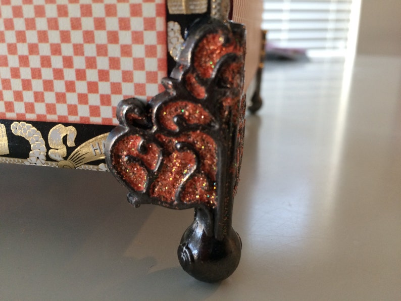 May include: A decorative black metal foot with an intricate design and a red glitter finish. The foot is round and has a ball-shaped base.