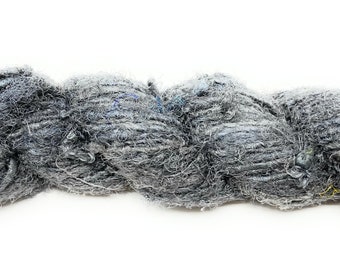 May include: A skein of gray yarn with a textured, slightly fuzzy appearance. The yarn is a mix of light and dark gray fibers, with subtle hints of blue and yellow. The yarn is tightly twisted, creating a thick, rope-like structure.