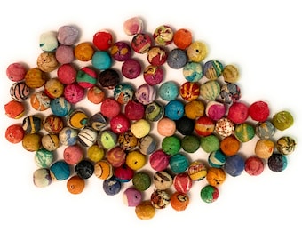 May include: A collection of colorful, fabric-covered beads in various sizes and patterns. The beads are primarily round, with a mix of solid colors and patterned fabrics, including stripes and floral designs. The color palette includes red, blue, yellow, and green.