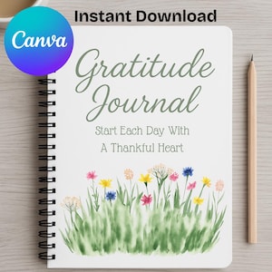 Może przedstawiać: Biały spiralny dziennik wdzięczności z napisem "Gratitude Journal" w zielonym skrypcie. Dziennik zawiera akwarelowy wzór kwiatów i trawy na dole. Ołówek spoczywa po prawej stronie.