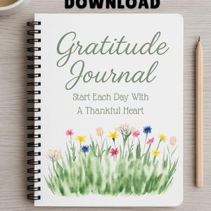 Może przedstawiać: Dziennik wdzięczności w oprawie spiralnej z białą okładką zawierającą napis "Gratitude Journal" oraz "Start Each Day With A Thankful Heart" w kolorze zielonym i szarym, ozdobiony akwarelową ilustracją zielonej trawy i kolorowych polnych kwiatów.