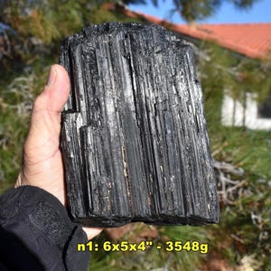 May include: A large, raw black tourmaline crystal held in a hand. The crystal is a deep black color with vertical striations. The dimensions are approximately 6 x 5 x 4 inches.