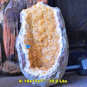 May include: A large, rough-edged geode with a hollow center filled with sparkling, golden-yellow crystals. The geode is approximately 18 inches long, 11 inches wide, and 7 inches deep, and weighs 39.9 lbs. The exterior is a mix of gray, white, and brown.