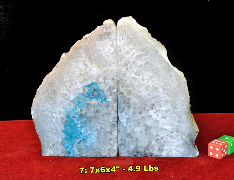 May include: Two natural agate bookends. Each bookend is a light gray color with a blue and white pattern. The bookends are 7 inches tall, 6 inches wide, and 4 inches deep, and weigh 4.9 pounds. A pair of dice are in the lower right corner.