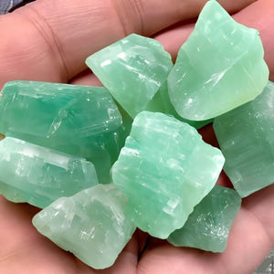 May include: A collection of green celestite crystal chunks. The crystals are translucent and have a light green color. The crystals are rough and have a natural, unpolished look.