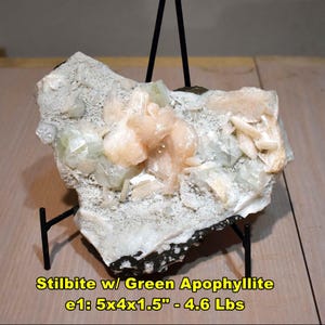 May include: A natural mineral specimen of Stilbite with Green Apophyllite. The stone features clusters of peach and pale green crystals on a matrix. The dimensions are approximately 5x4x1.5 inches and weighs 4.6 lbs. The text "Stilbite w/ Green Apophyllite" is visible.