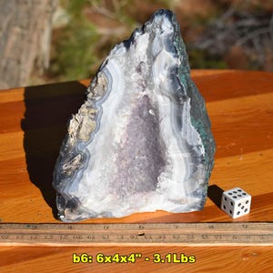 May include: A large, open geode with a crystalline interior, showcasing bands of white, gray, and purple. The exterior has dark gray and green hues. The geode is approximately 6 inches long, 4 inches wide, and 4 inches high, and weighs 3.1 pounds.