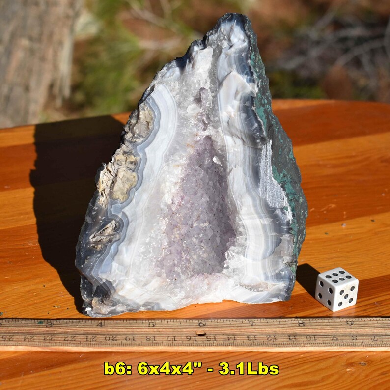 May include: A large, open geode with a crystalline interior, showcasing bands of white, gray, and purple. The exterior has dark gray and green hues. The geode is approximately 6 inches long, 4 inches wide, and 4 inches high, and weighs 3.1 pounds.