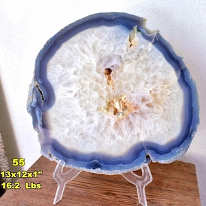 May include: A large, circular agate slice featuring concentric bands of deep blue and translucent white, with a central crystalline geode cavity. The specimen measures 13x12x1 inches and weighs 16.2 lbs, displayed on a clear acrylic stand.