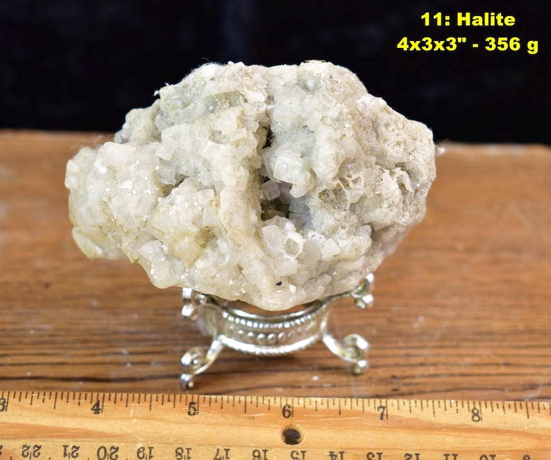 May include: A light-colored halite specimen, approximately 4x3x3 inches, displayed on a decorative silver stand. The mineral has a rough, textured surface. The image includes the text "11: Halite 4x3x3" - 356 g".