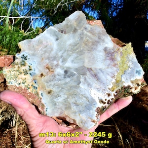 May include: A large quartz geode with amethyst inclusions. The rock is approximately 6 x 6 x 2 inches and weighs 2245 grams. The geode features a mix of white, purple, and green colors, with a rough, textured surface.