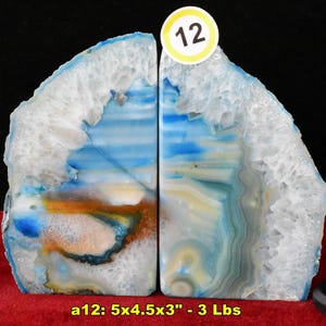 May include: A pair of blue and white agate bookends with crystalline edges and banded patterns. The stones feature natural layers of blue, white, and brown. A circular sticker with the number 12 is attached. Dimensions are 5x4.5x3 inches and 3 lbs.