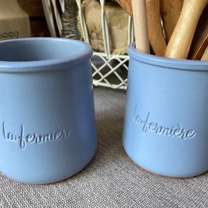 May include: Two light blue ceramic utensil holders with the word "la fermiere" embossed on the front.
