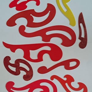 May include: A collection of nine French curve drafting templates in various shapes. Eight of the templates are red, and one is yellow. These flat, plastic drawing tools feature smooth, irregular curved edges designed for creating precise technical curves.