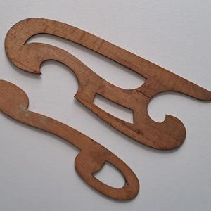 May include: Two light brown wooden French curves with smooth, sanded surfaces and distinct, irregular geometric cutouts. These drafting tools feature curved edges and pointed ends, showcasing the natural wood grain and texture throughout.
