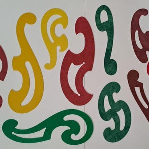 May include: A collection of nine French curve drafting templates in various shapes and sizes. The set includes pieces in solid red, yellow, and green, featuring smooth, irregular curved edges and internal cutouts for drawing precise curves.