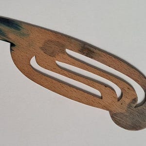 Op de afbeelding: Een platte, langwerpige houten boekenlegger met een natuurlijke lichtbruine nerf en donkerblauw-grijze gebeitste accenten aan beide uiteinden. Het object heeft een gladde, gebogen vorm met twee parallelle uitsparingen in het midden.