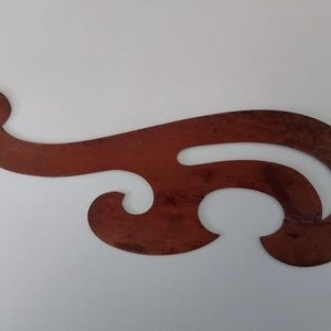 May include: A brown wooden French curve drafting tool featuring a smooth, irregular, flowing shape with multiple curved edges and a central cutout, designed for drawing complex curves in technical drafting and pattern making projects.