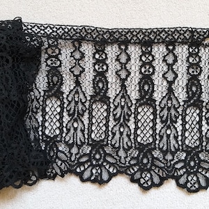 Può includere: Tessuto di pizzo nero con un intricato motivo floreale e geometrico. Il pizzo è piegato, rivelando il dettagliato design traforato. I bordi sono smerlati, aggiungendo un tocco delicato a questo tessuto.