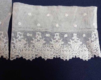 Puede incluir: Borde de encaje blanco con un delicado diseño floral y pequeños puntos. El encaje está cosido sobre una tela transparente.