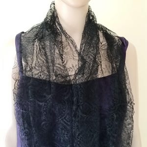 May include: A black lace scarf draped over a dark blue garment. The delicate lace creates a layered effect, with intricate patterns visible. The scarf adds a touch of elegance and texture to the outfit.