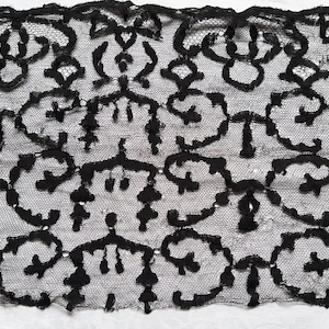 Può includere: Primo piano di tessuto di pizzo nero con un intricato motivo floreale. Il pizzo presenta un delicato design a trama aperta con motivi ripetuti. Il nero offre un contrasto sorprendente, evidenziando la texture dettagliata del tessuto. Ideale per progetti di cucito.