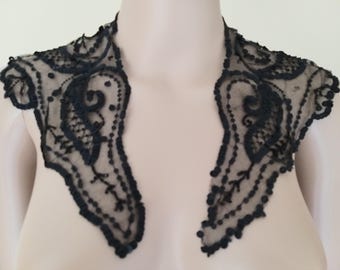 May include: A black lace collar featuring detailed floral and dot patterns. The delicate, openwork design is displayed on a mannequin, highlighting the collar's shape and detail. This vintage-inspired accessory adds a touch of elegance.