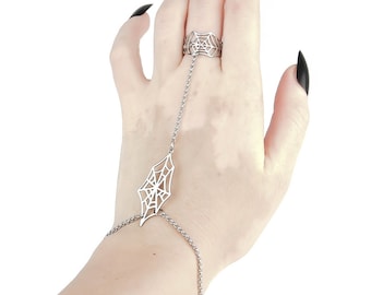 May include: A silver spiderweb ring with a chain that extends to the wrist, forming a bracelet. The ring and bracelet are both detailed with a spiderweb design.