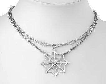 May include: A silver necklace with a spiderweb pendant. The necklace is layered with two chains.