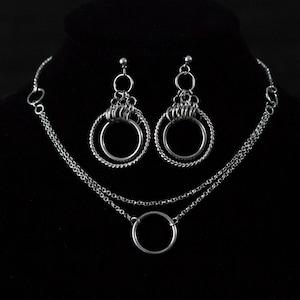 Può includere: Una collana d'argento con due catene e un ciondolo circolare grande, e un paio di orecchini d'argento con più cerchi.
