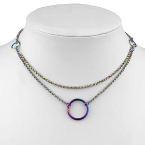 Op de afbeelding: Een gelaagde ketting met een regenboogkleurige, iriserende afwerking. De ketting heeft een dunne ketting met een grotere cirkelhanger.
