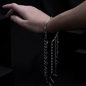 Può includere: Un braccialetto d'argento con più catene pendenti. Il braccialetto è al polso di una persona e le catene pendono verso il basso.