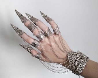 May include: A silver claw ring set with intricate filigree designs and dangling chains. The set includes multiple rings for each finger and a matching bracelet.