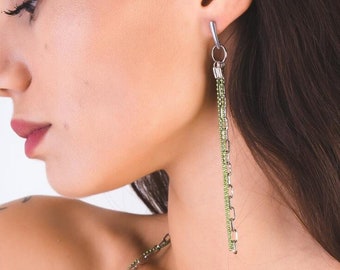 May include: A woman wearing a silver chain necklace with a green beaded chain layered on top. She is also wearing long green beaded earrings.