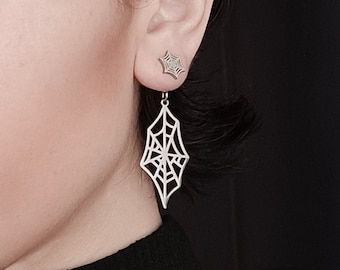 May include: A woman with short, dark hair wearing a black turtleneck sweater. She has black eyeliner and a spiderweb-shaped earring in her left ear.