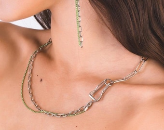 May include: A woman wearing a silver chain necklace with a green beaded chain layered on top. She is also wearing long green beaded earrings.