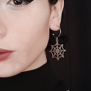 A poised model showcases Myril Jewels' half hoop spiderweb earrings, embodying a dark avant-garde aesthetic. Perfect for gothic and alternative fashion enthusiasts, add a touch of neo-gothic outfit