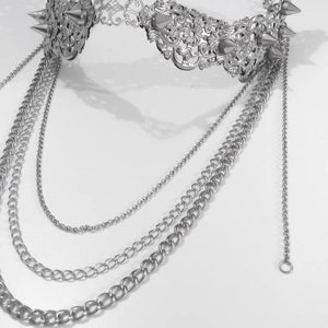 Puede incluir: Un collar de cadena de plata con una pieza central decorativa, adornada y con p&uacute;as. El collar tiene varias cadenas de diferentes longitudes.