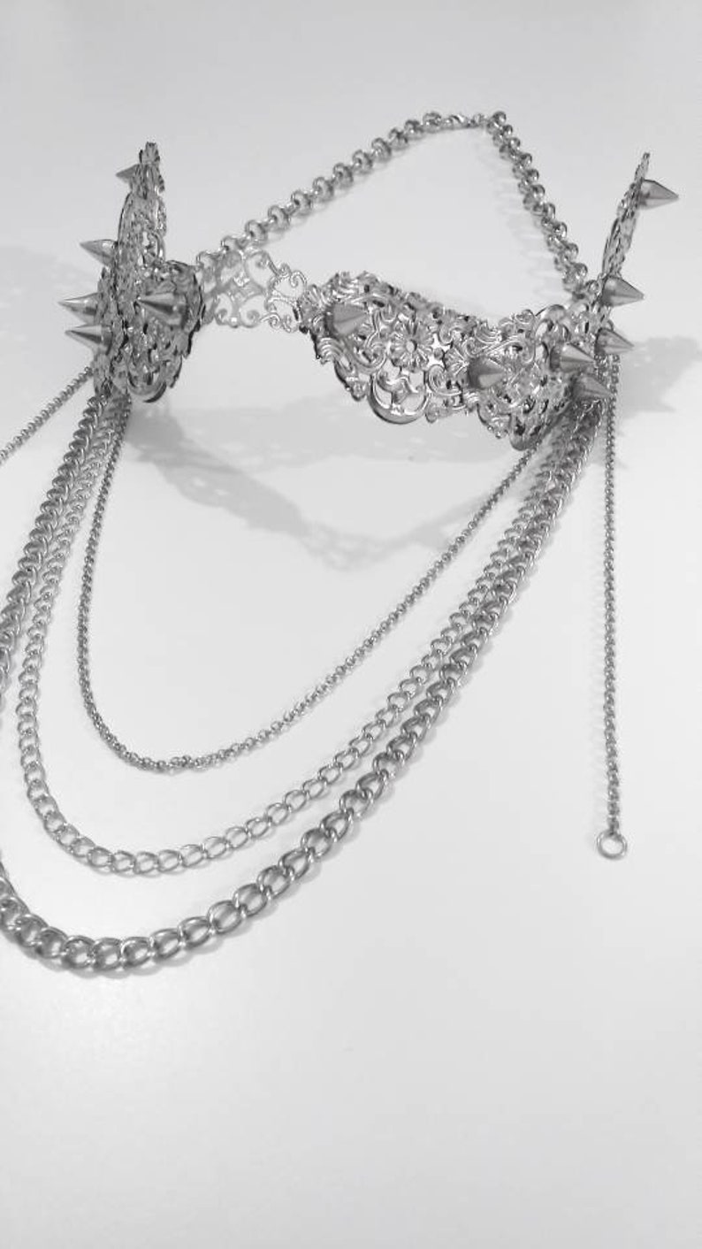 Puede incluir: Un collar de cadena de plata con una pieza central decorativa, adornada y con p&uacute;as. El collar tiene varias cadenas de diferentes longitudes.