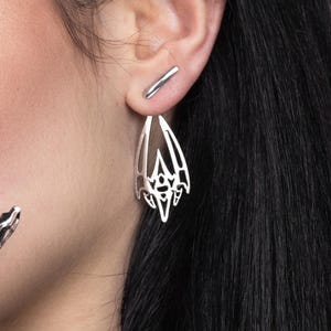 Può includere: Orecchini d'argento con un design delicato e intricato che ricorda un'ala di pipistrello. Gli orecchini sono pendenti e hanno un'estetica minimalista e moderna.